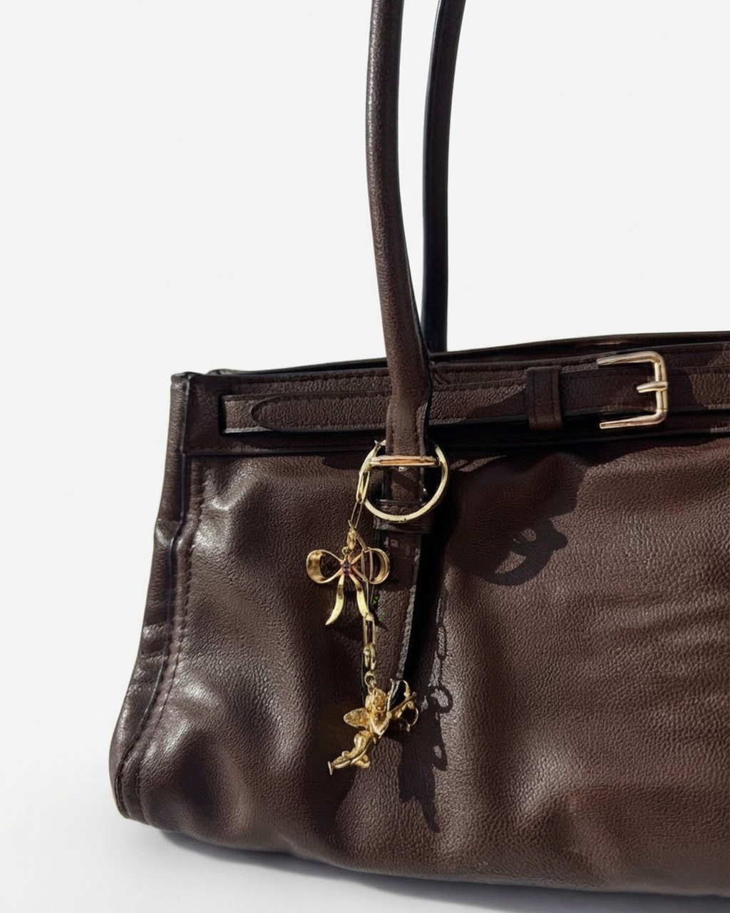 Gold Bag Bit - Dunkelbraune Ledertasche mit einer feinen, herabhängenden goldenen Kette, die mit einer Schleife und einem Engel-Anhänger verziert ist.