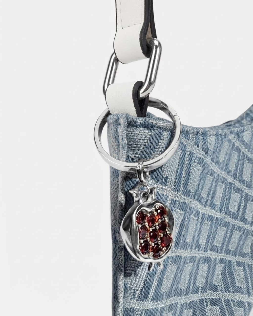 Silber Bag Bit - Nahaufnahme einer blau-gemusterte Denim-Tasche mit einem weißen Schulterriemen und daran einen silbernen Granatapfel-Anhänger befestigt.