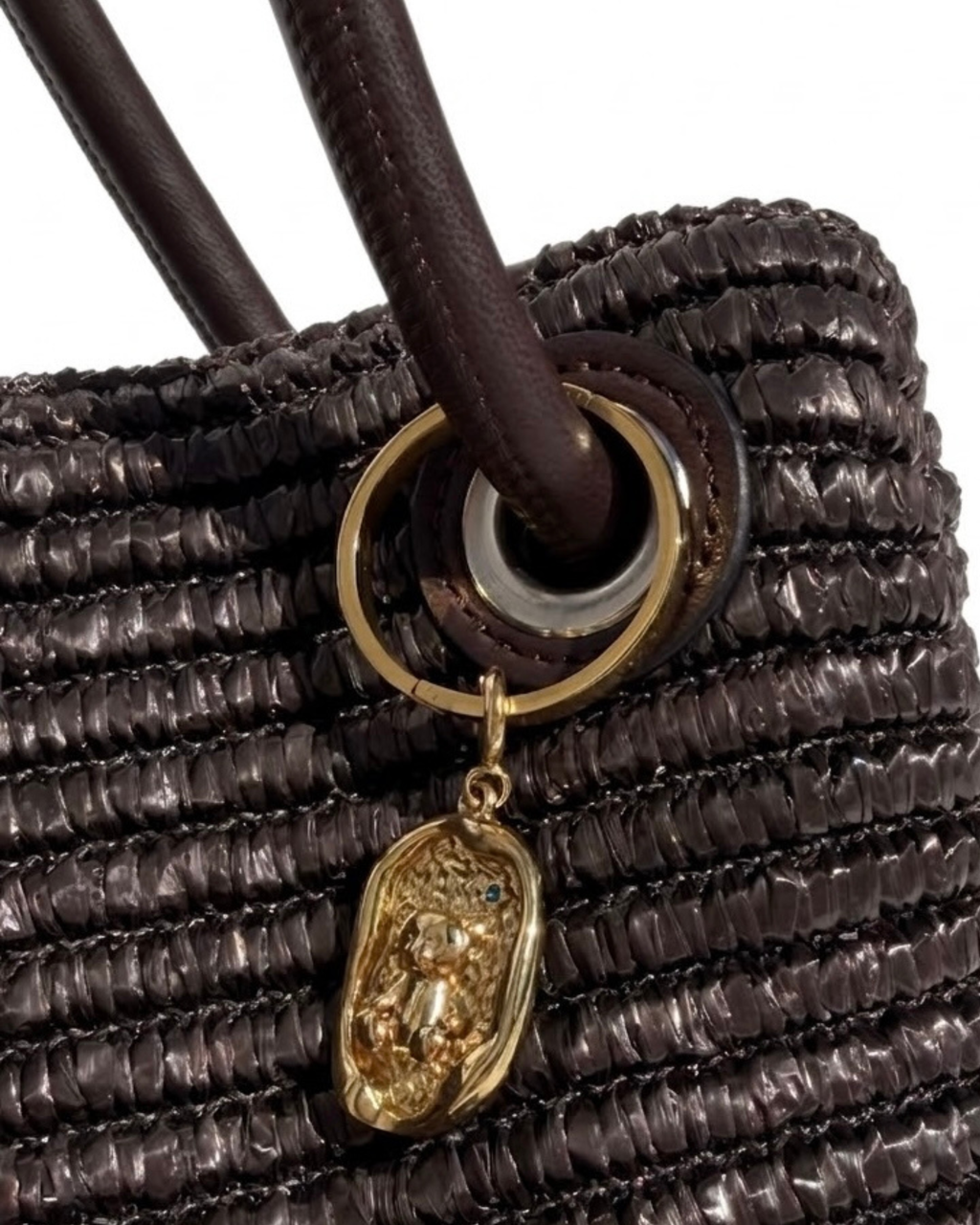 Gold BagBit - Nahaufnahme einer dunkelbraunen, strukturierten Tasche, verziert mit einem ovalen, goldenen Anhänger, der einen kleinen Teddybären in einem strukturierten Relief zeigt.