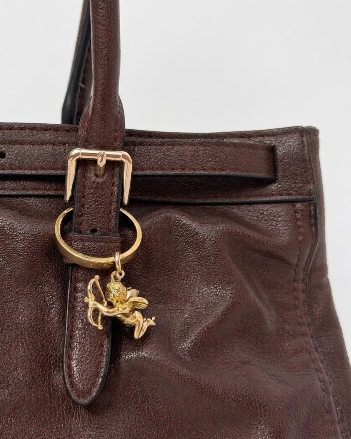 Gold BagBit -  Nahaufnahme einer dunkelbraunen Ledertasche, verziert mit einem detaillierten goldenen Cupid-Anhänger.