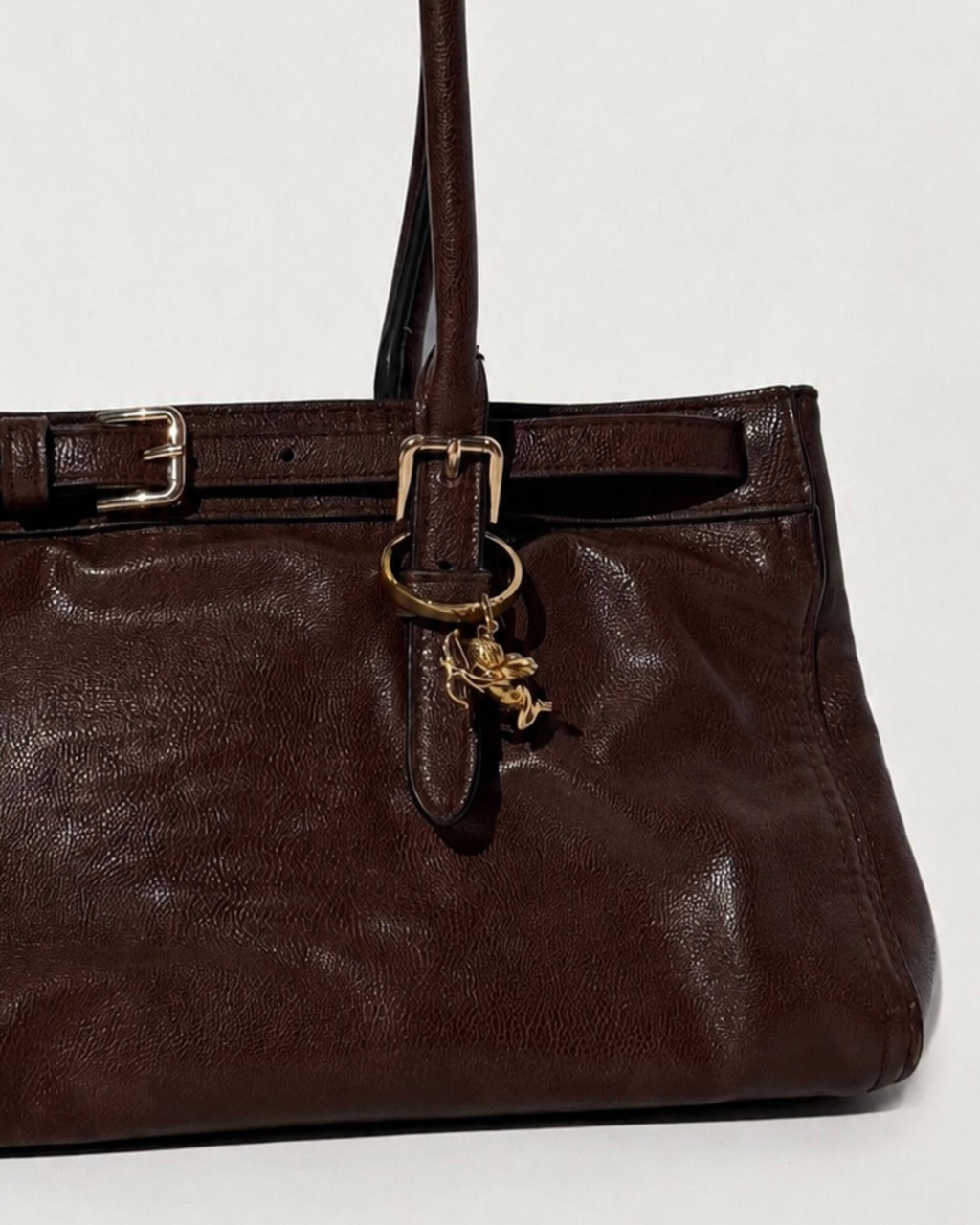 Gold BagBit -  Aufnahme einer dunkelbraunen Ledertasche, verziert mit einem detaillierten goldenen Cupid-Anhänger.