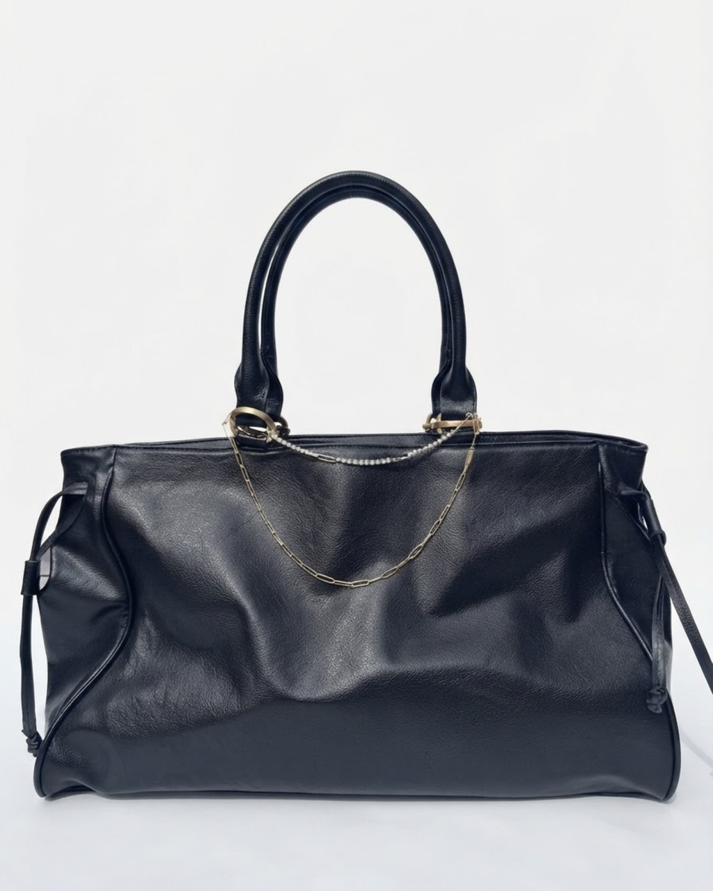 Gold Mixed Duo Chain - Schwarze Handtasche aus Leder mit zwei goldenen Ketten (eine Strasskette oben und eine klassische Kette darunter) zwischen den Henkeln gespannt vor neutralem Hintergrund.