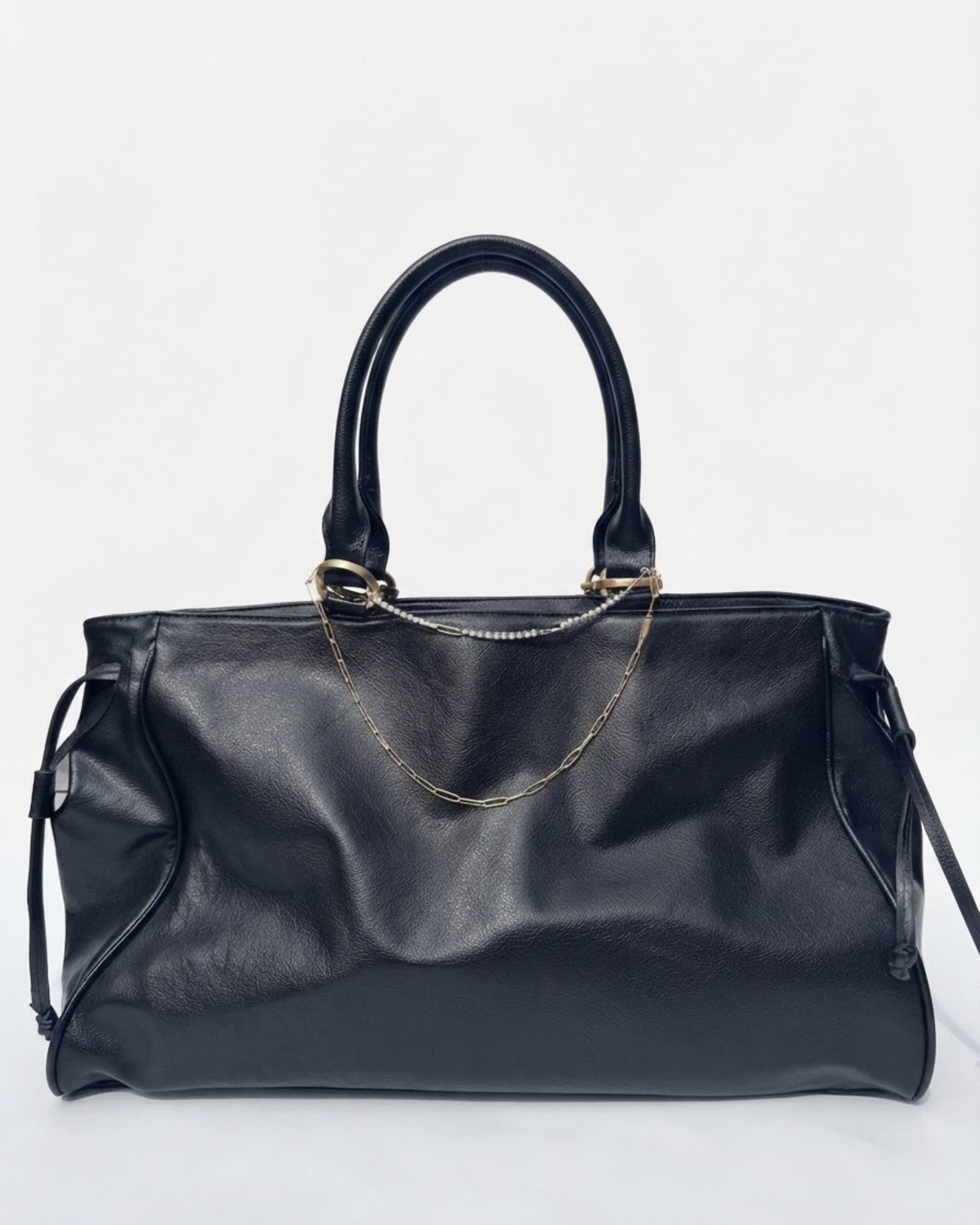Gold Mixed Duo Chain - Schwarze Handtasche aus Leder mit zwei goldenen Ketten (eine Strasskette oben und eine klassische Kette darunter) zwischen den Henkeln gespannt vor neutralem Hintergrund.