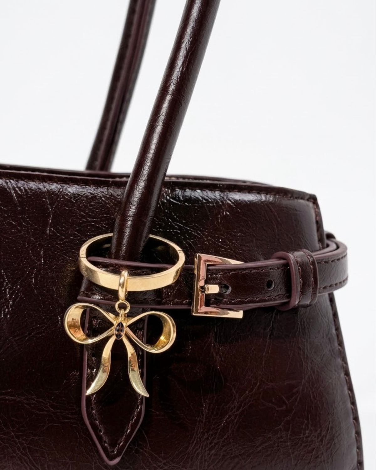 Gold BagBit - Nahaufnahme einer dunkelroten, glänzenden Ledertasche, verziert mit einem goldenen Schleifenanhänger, der einen kleinen braunen Stein in der Mitte hält.