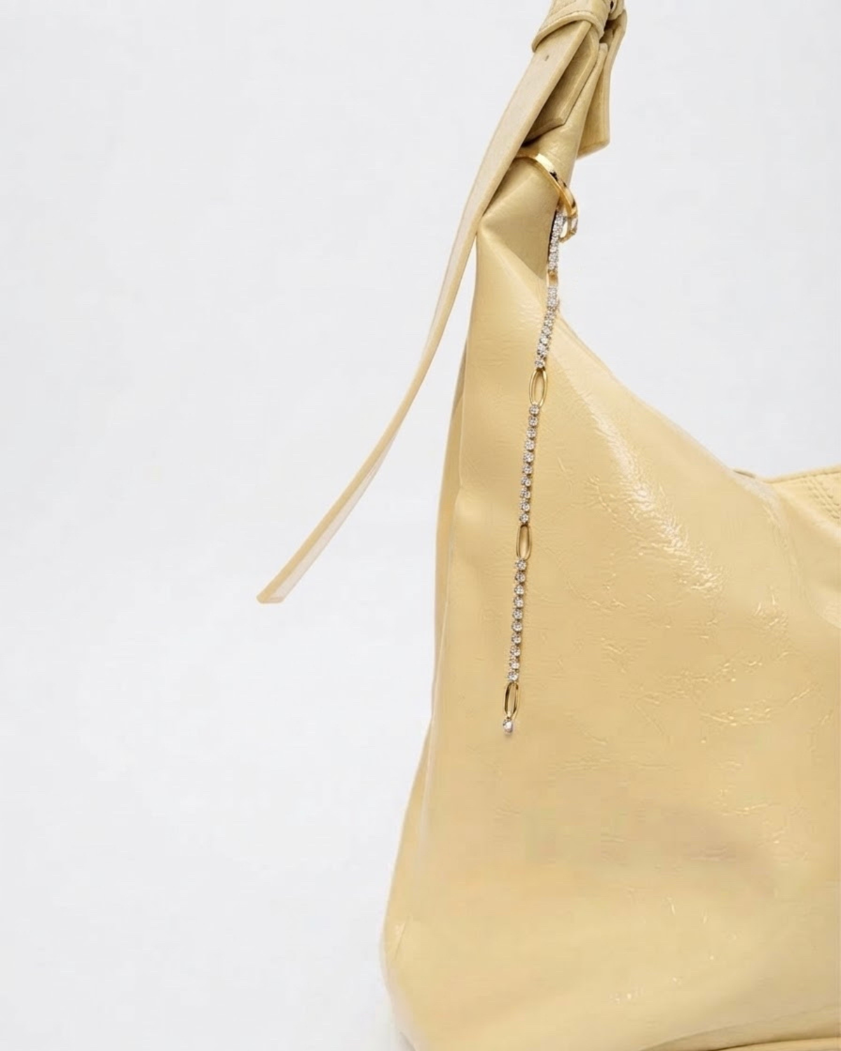 Gold Strass Single Chain - Hellgelbe Schultertasche aus glänzendem Leder mit einer feinen Strasskette am Henkel, welche regelmäßig durch goldene, ovale Kettenglieder unterbrochen wird.