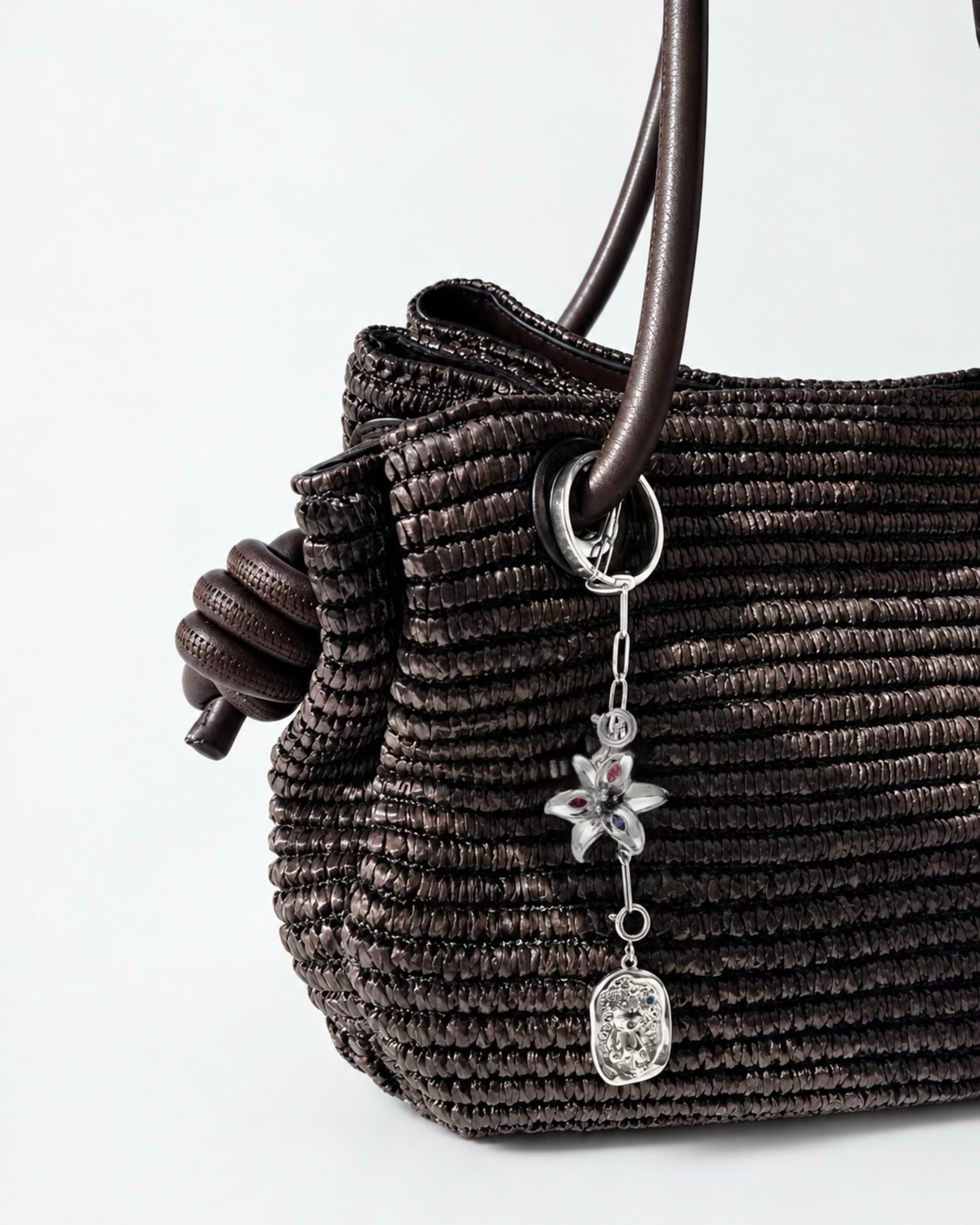 Silber Bag Bit - Dunkelbraune Tasche mit einer kurzen, herabhängenden silberfarbenen Kette, verziert mit einer Blume und einem Teddybär-Medaillon.