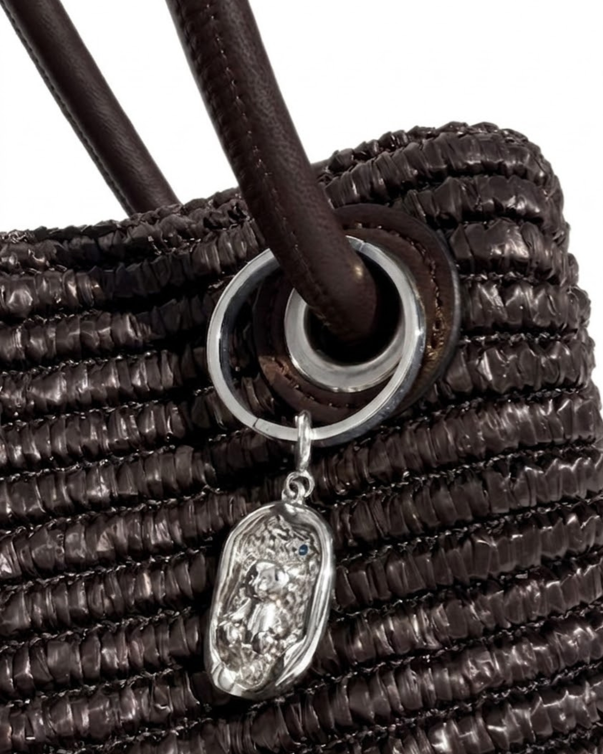 Silber BagBit - Nahaufnahme einer dunkelbraunen, strukturierten Tasche, verziert mit einem ovalen, silberner Anhänger, der einen kleinen Teddybären in einem strukturierten Relief zeigt. 