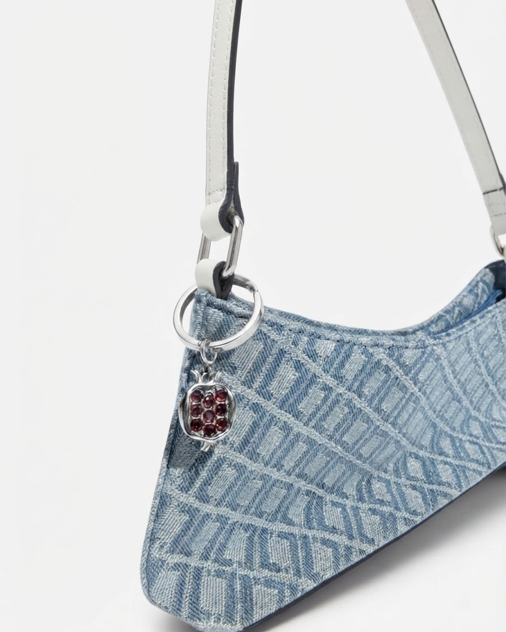 Silber Bag Bit - Blau-gemusterte Denim-Schultertasche mit weißem Riemen und daran einen silbernen Granatapfel-Anhänger befestigt.