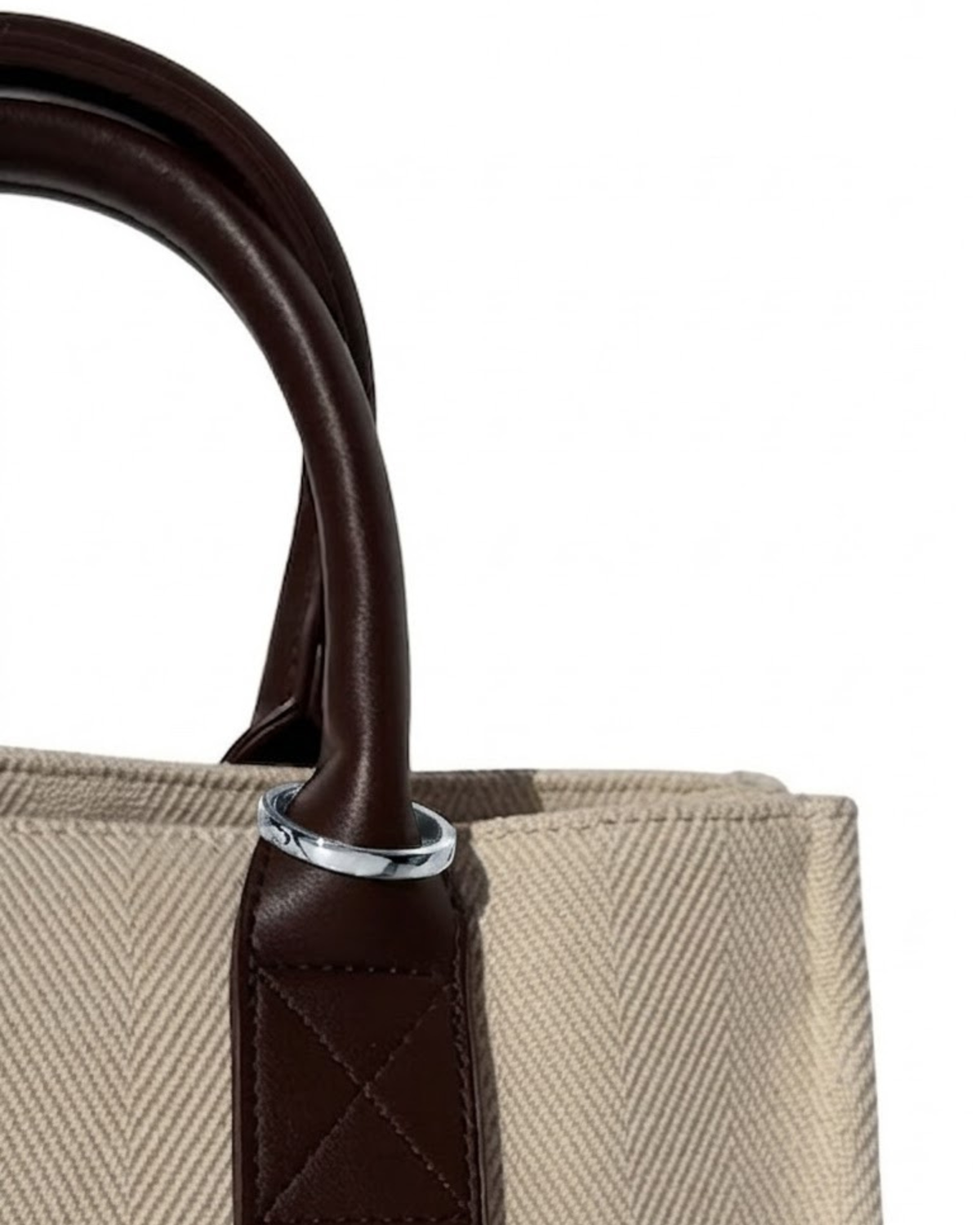 Silber Bag Clip - Nahaufnahme einer beigefarbenen Canvas-Tasche mit Griffen aus dunkelbraunem Leder, geschmückt mit einem silbernen Metallring.