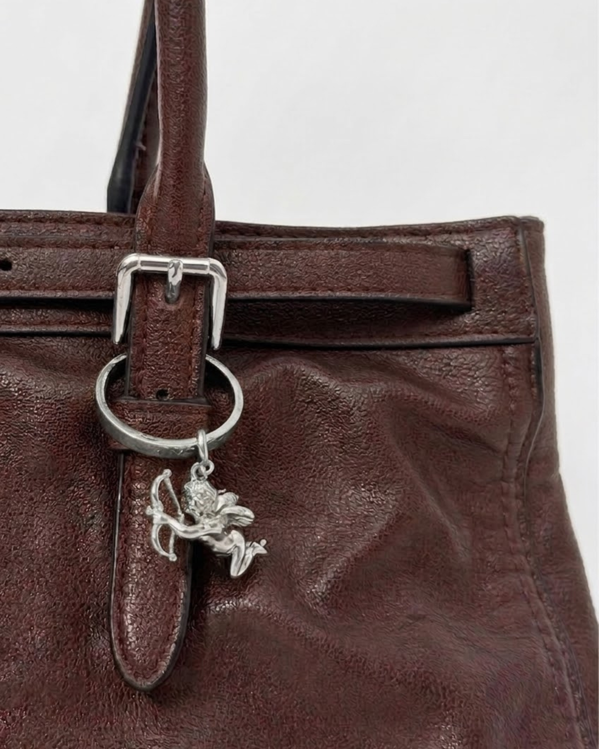 Silber BagBit - Nahaufnahme einer dunkelbraunen Ledertasche, verziert mit einem detaillierten silbernen Cupid-Anhänger.