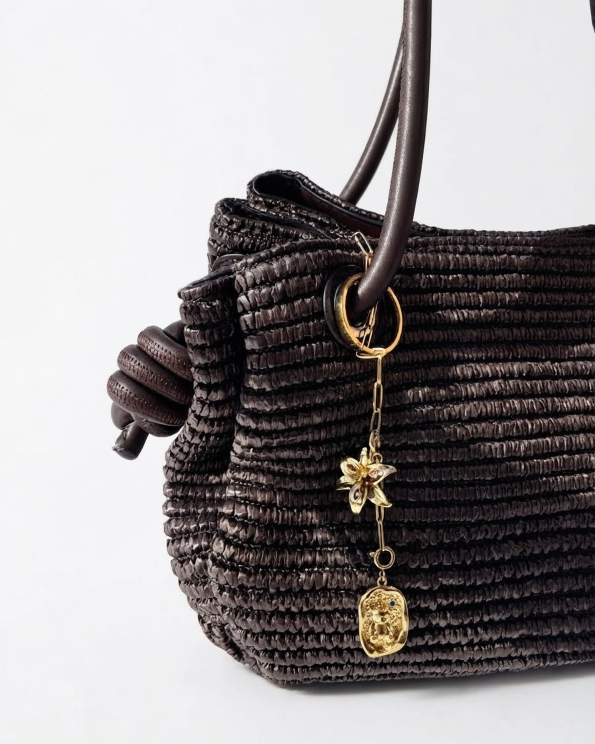 Gold Bag Bit - Dunkelbraune Tasche mit einer kurzen, herabhängenden goldfarbenen Kette, verziert mit einer Blume und einem Teddybär-Medaillon.