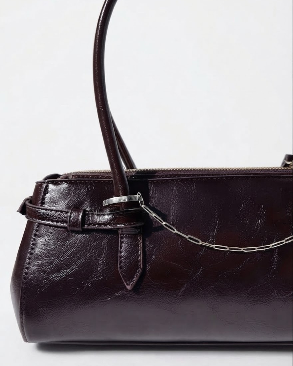 Silber Bag Chain - Dunkelrote Schultertasche aus glänzendem Leder mit einer feinen, silberfarbenen Gliederkette als Detail zwischen den beiden Henkeln gespannt.