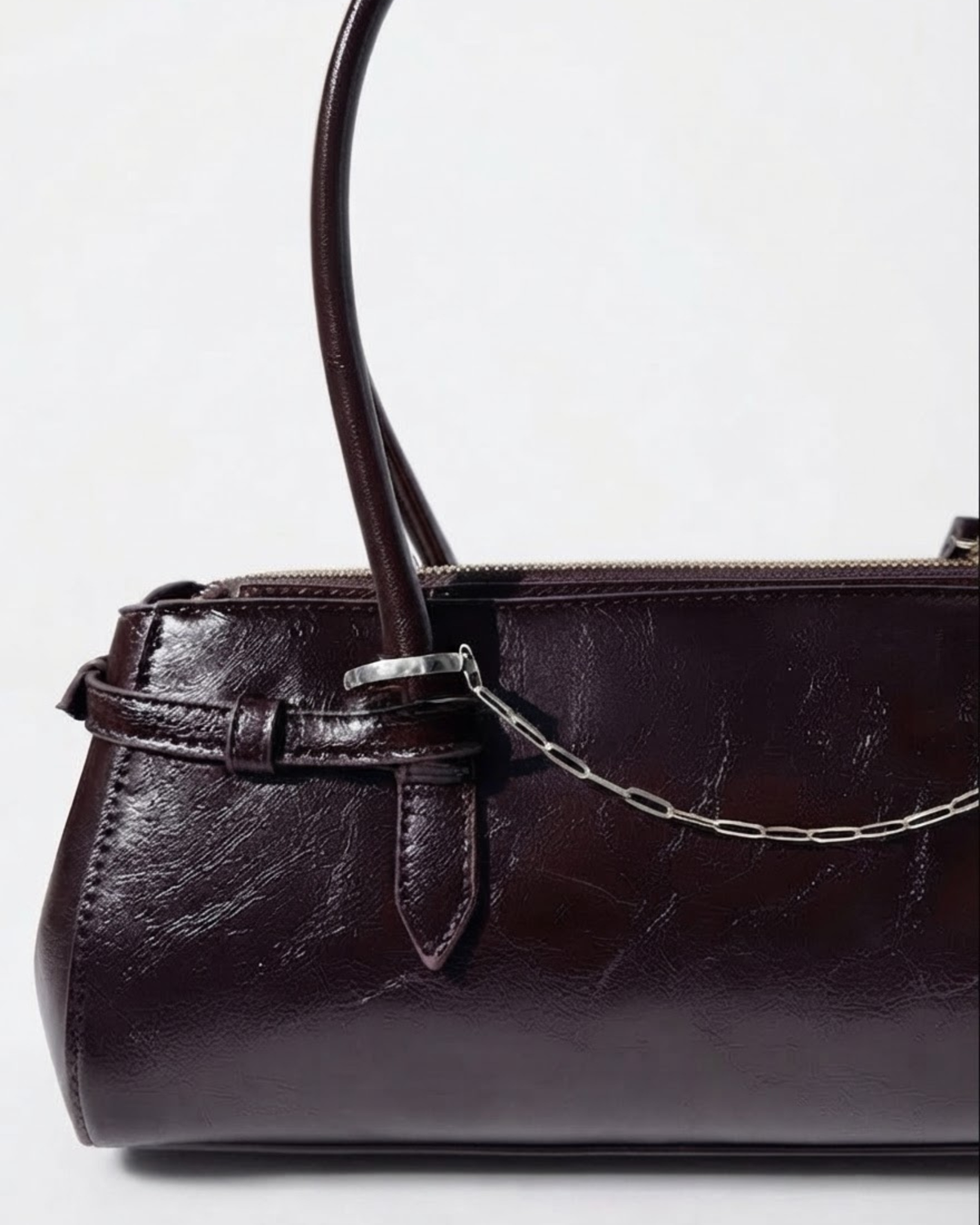 Silber Bag Chain - Dunkelrote Schultertasche aus glänzendem Leder mit einer feinen, silberfarbenen Gliederkette als Detail zwischen den beiden Henkeln gespannt.