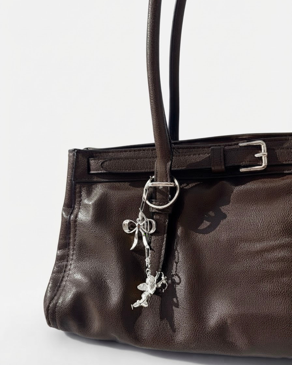 Silber Bag Bit - Dunkelbraune Ledertasche mit einer feinen, herabhängenden silbernen Kette, die mit einer Schleife und einem Engel-Anhänger verziert ist.