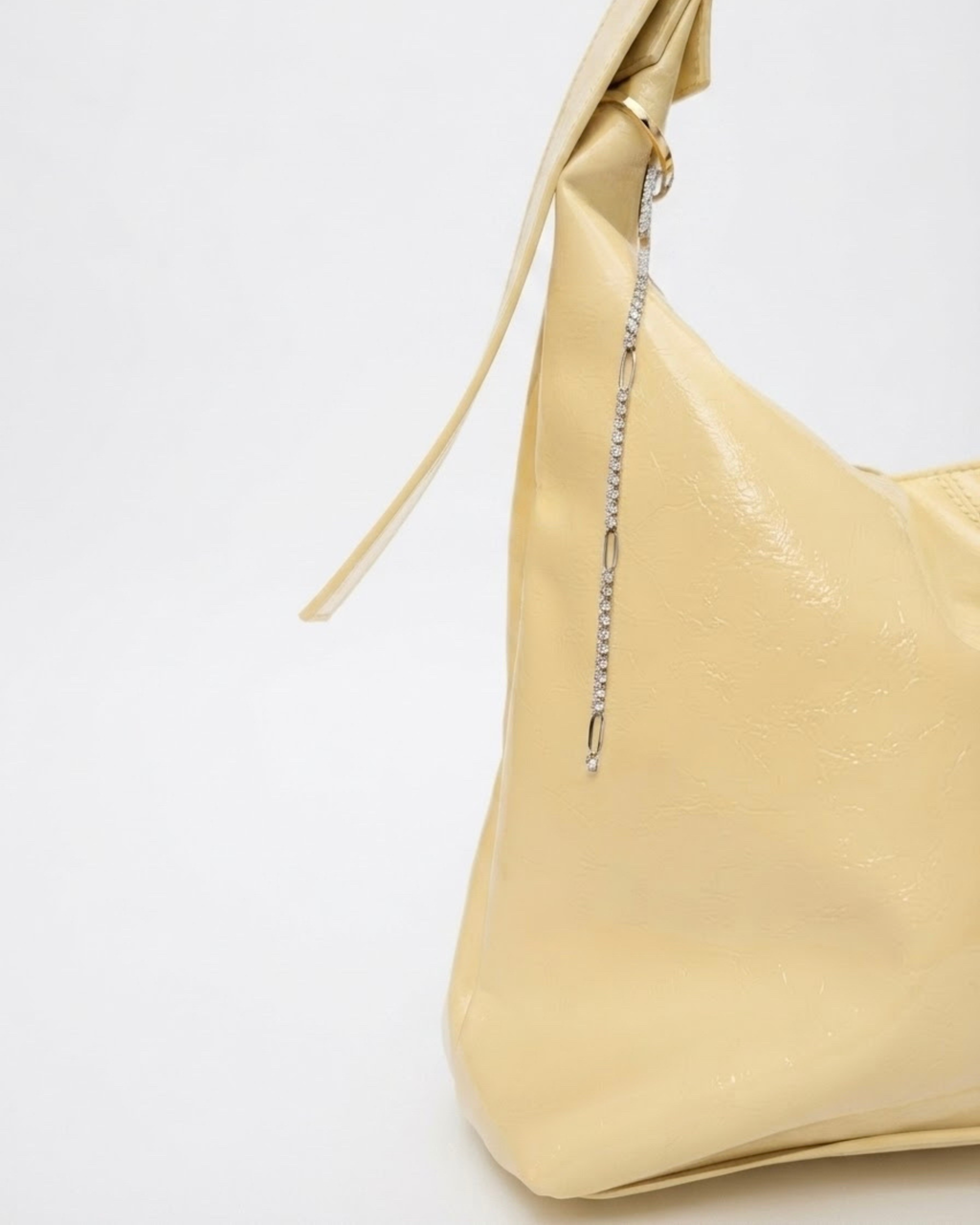 Silber Strass Single Chain - Hellgelbe Schultertasche aus glänzendem Leder mit einer feinen Strasskette am Henkel, welche regelmäßig durch silberne, ovale Kettenglieder unterbrochen wird.