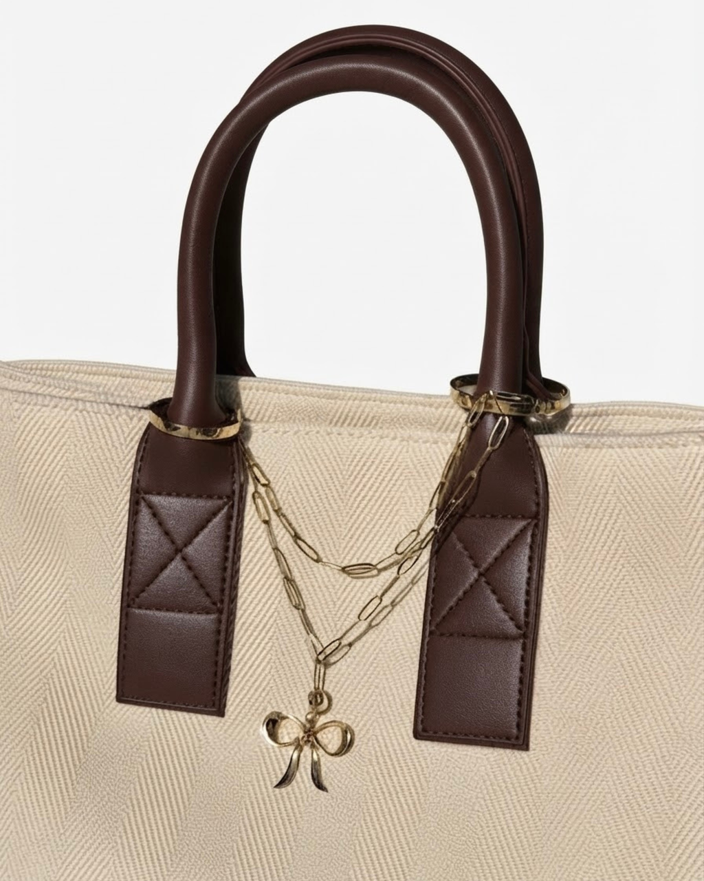 Gold Bag Chain - Beige-cremefarbene Tasche mit braunen Ledergriffen, verziert mit einer doppelreihigen, goldfarbenen Kette und einem zentralen Schleifenanhänger.