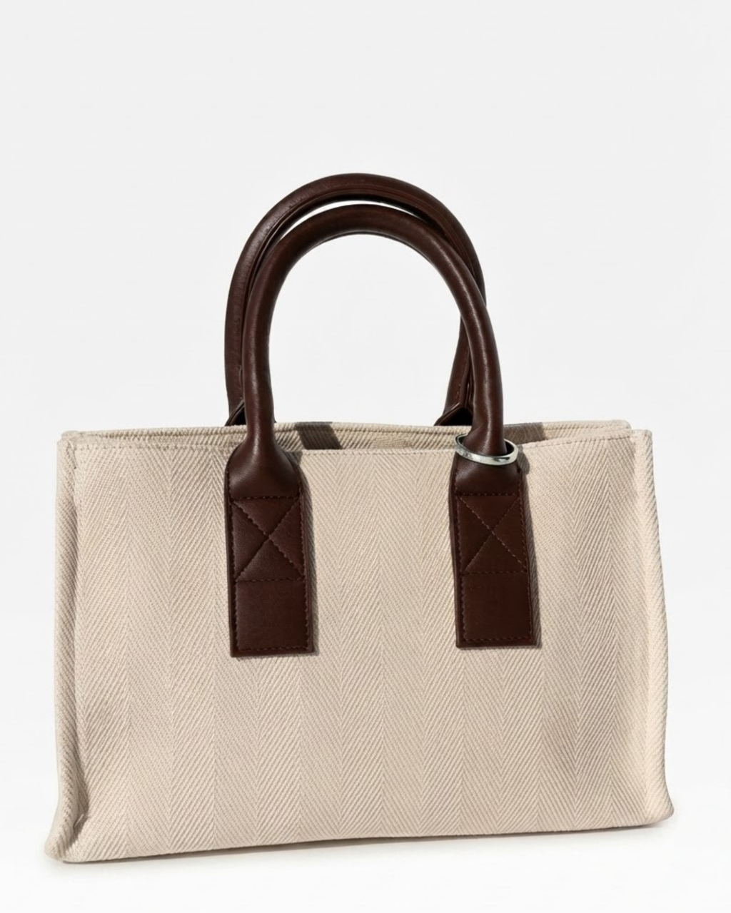 Silber Bag Clip - Aufnahme einer beigefarbenen Canvas-Tasche mit Griffen aus dunkelbraunem Leder, geschmückt mit einem silbernen Metallring.