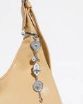 Silber Bag Charm - Nahaufnahme einer gelben Handtasche mit einem herabhängenden, mehrteiligen Silberanhänger, bestehend aus einem Herz, einer Motte auf weißem Emaille und einem runden Medaillon.