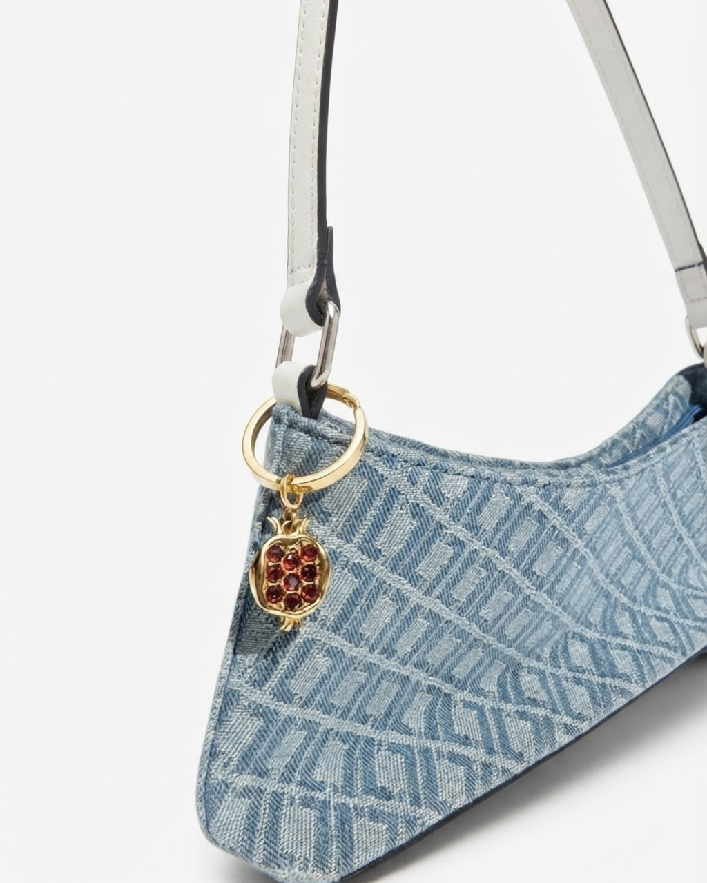 Gold Bag Bit - Blau-gemusterte Denim-Schultertasche mit weißem Riemen und daran einen goldenen Granatapfel-Anhänger befestigt.