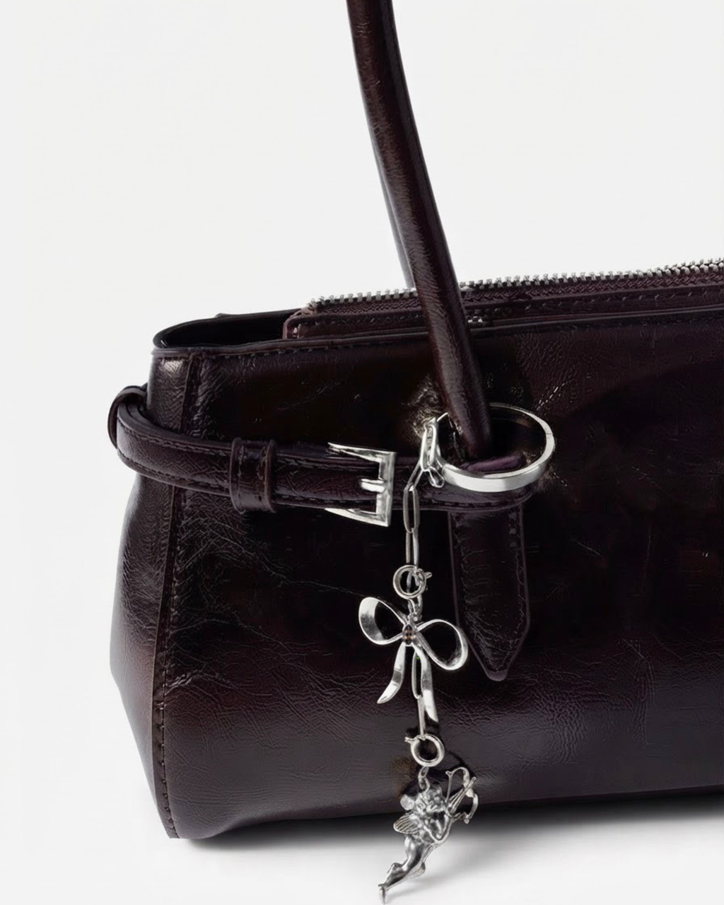 Silber Bag Bit - Dunkelrote Schultertasche aus glänzendem Leder mit einer kurzen, herabhängenden silbernen Kette, dekoriert mit einer Schleife und einem Engel-Anhänger.
