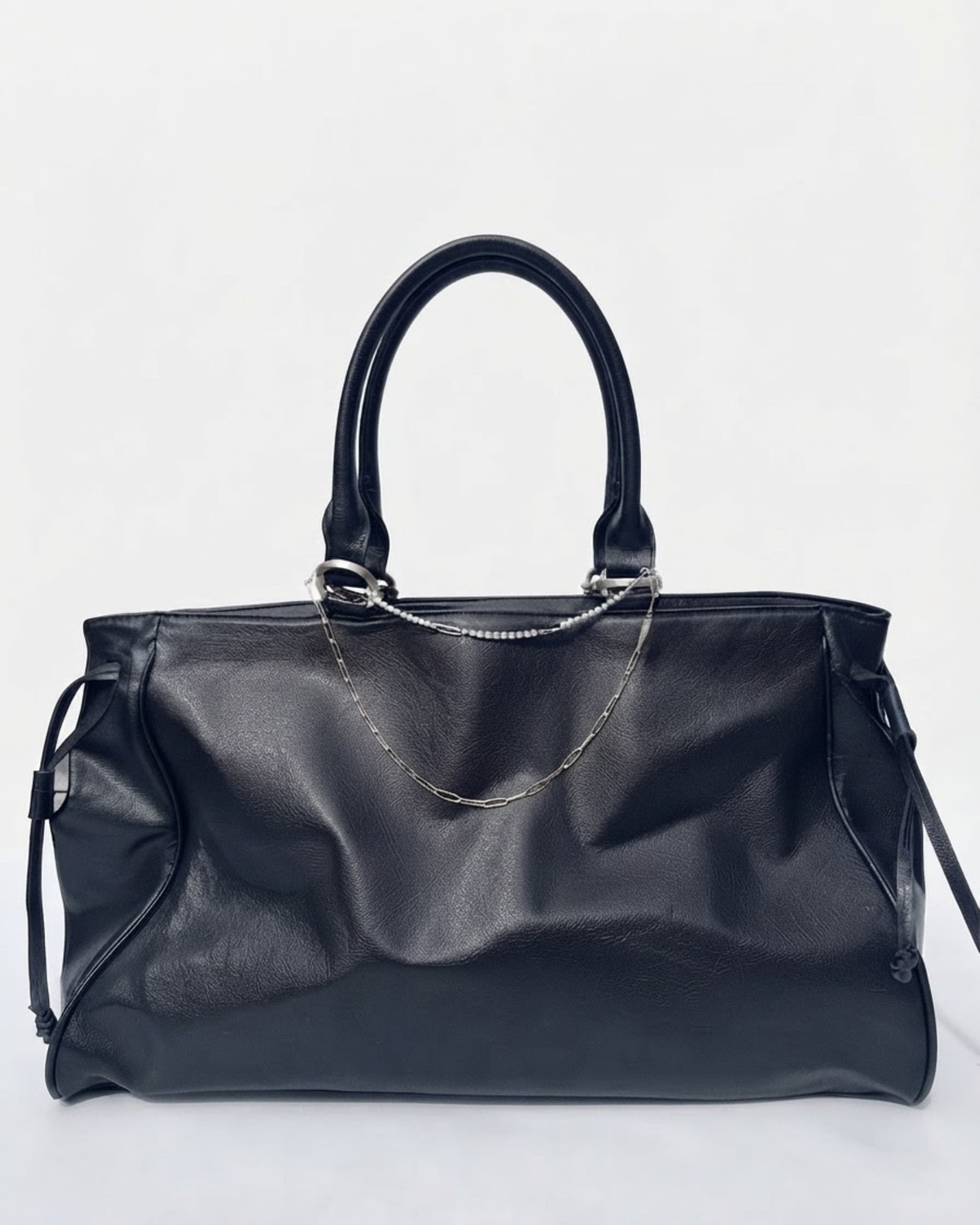 Silber Mixed Duo Chain - Schwarze Handtasche aus Leder mit zwei silbernen Ketten (eine Strasskette oben und eine klassische Kette darunter) zwischen den Henkeln gespannt vor neutralem Hintergrund.