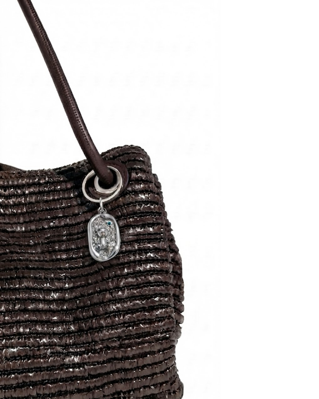 Silber BagBit - Aufnahme einer dunkelbraunen, strukturierten Tasche, verziert mit einem ovalen, silberner Anhänger, der einen kleinen Teddybären in einem strukturierten Relief zeigt.