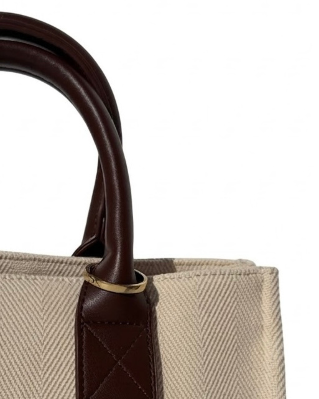Gold Bag Clip - Nahaufnahme einer beigefarbenen Canvas-Tasche mit Griffen aus dunkelbraunem Leder, geschmückt mit einem goldenen Metallring.