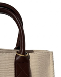 Gold Bag Clip - Nahaufnahme einer beigefarbenen Canvas-Tasche mit Griffen aus dunkelbraunem Leder, geschmückt mit einem goldenen Metallring.