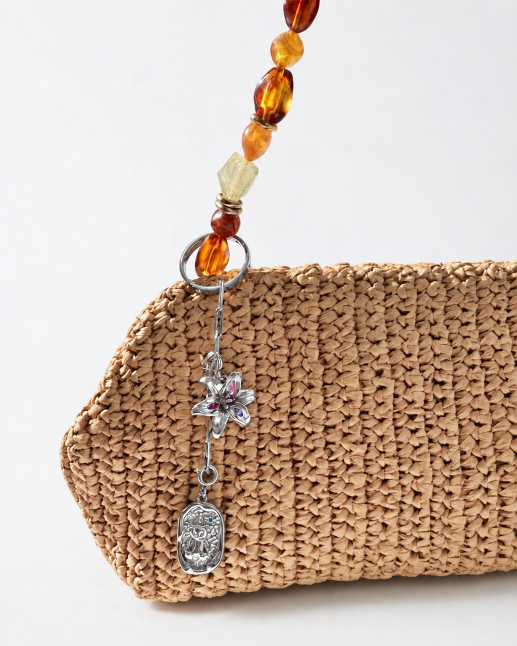 Silber Bag Bit - Beigefarbene Tasche mit einer kurzen silbernen Kette mit Blumen- und Medaillon-Anhänger am Taschenhenkel befestigt.