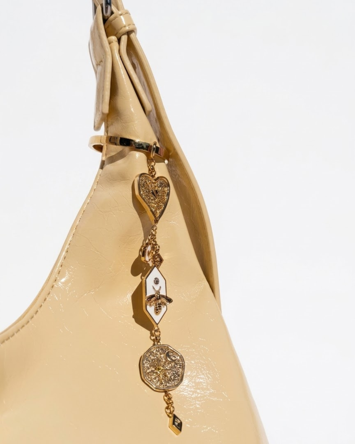 Gold Bag Charm - Nahaufnahme einer gelben Handtasche mit einem herabhängenden, mehrteiligen Goldanhänger, bestehend aus einem Herz, einer Motte auf weißem Emaille und einem runden Medaillon.