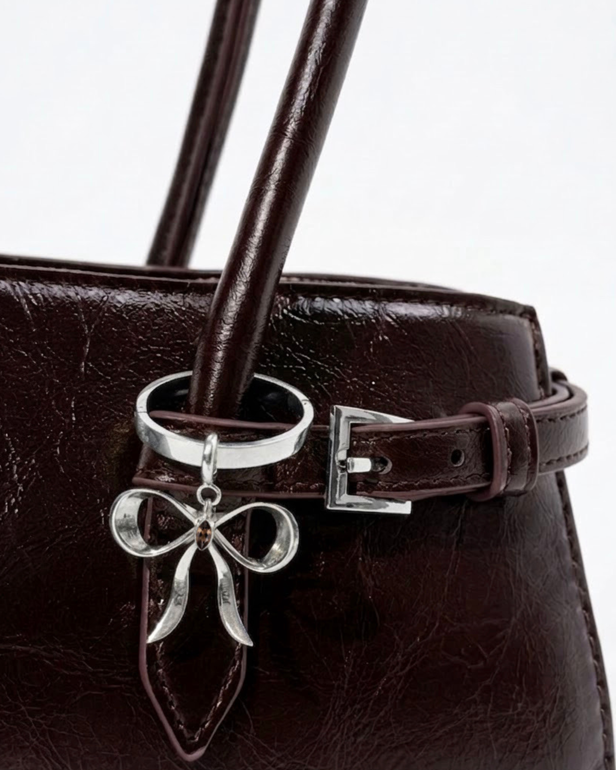 Silber BagBit - Nahaufnahme einer dunkelroten, glänzenden Ledertasche, verziert mit einem silbernen Schleifenanhänger, der einen kleinen braunen Stein in der Mitte hält. 