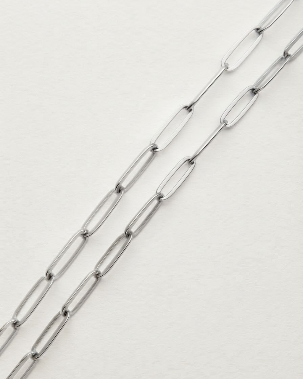 Silber Bag Chain - Nahaufnahme von zwei parallelen, silberfarbenen Ketten mit länglichen Gliedern, die diagonal über einen weißen Hintergrund verlaufen.