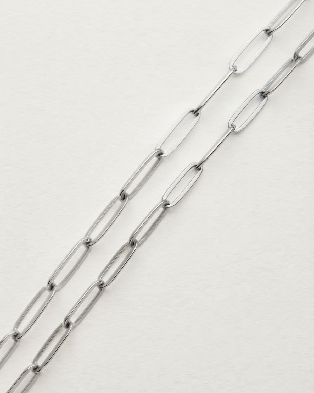 Silber Bag Chain - Nahaufnahme von zwei parallelen, silberfarbenen Ketten mit länglichen Gliedern, die diagonal über einen weißen Hintergrund verlaufen.