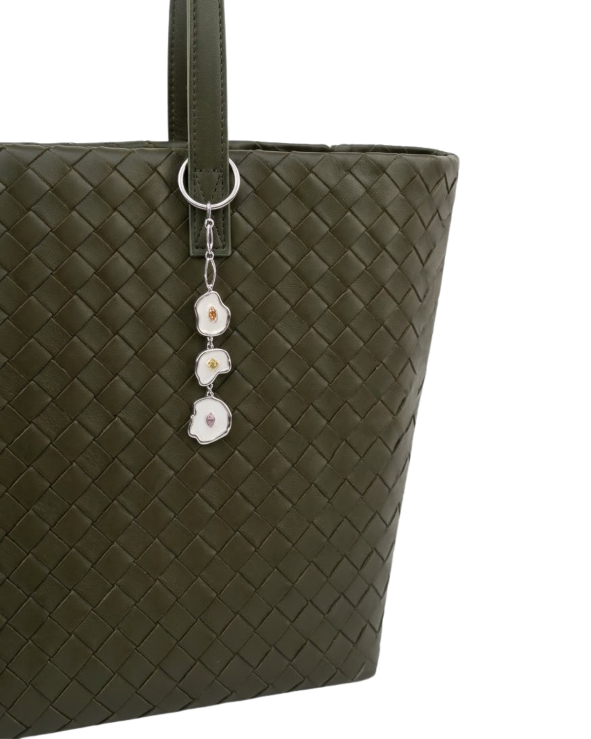 Silber Bag Charm -  Aufnahme einer olivgrünen, geflochtenen Leder-Handtasche, verziert mit einem herabhängenden Anhänger aus drei unregelmäßig geformten, silberumrandeten Emaille-Elementen mit kleinen Schmucksteinen.