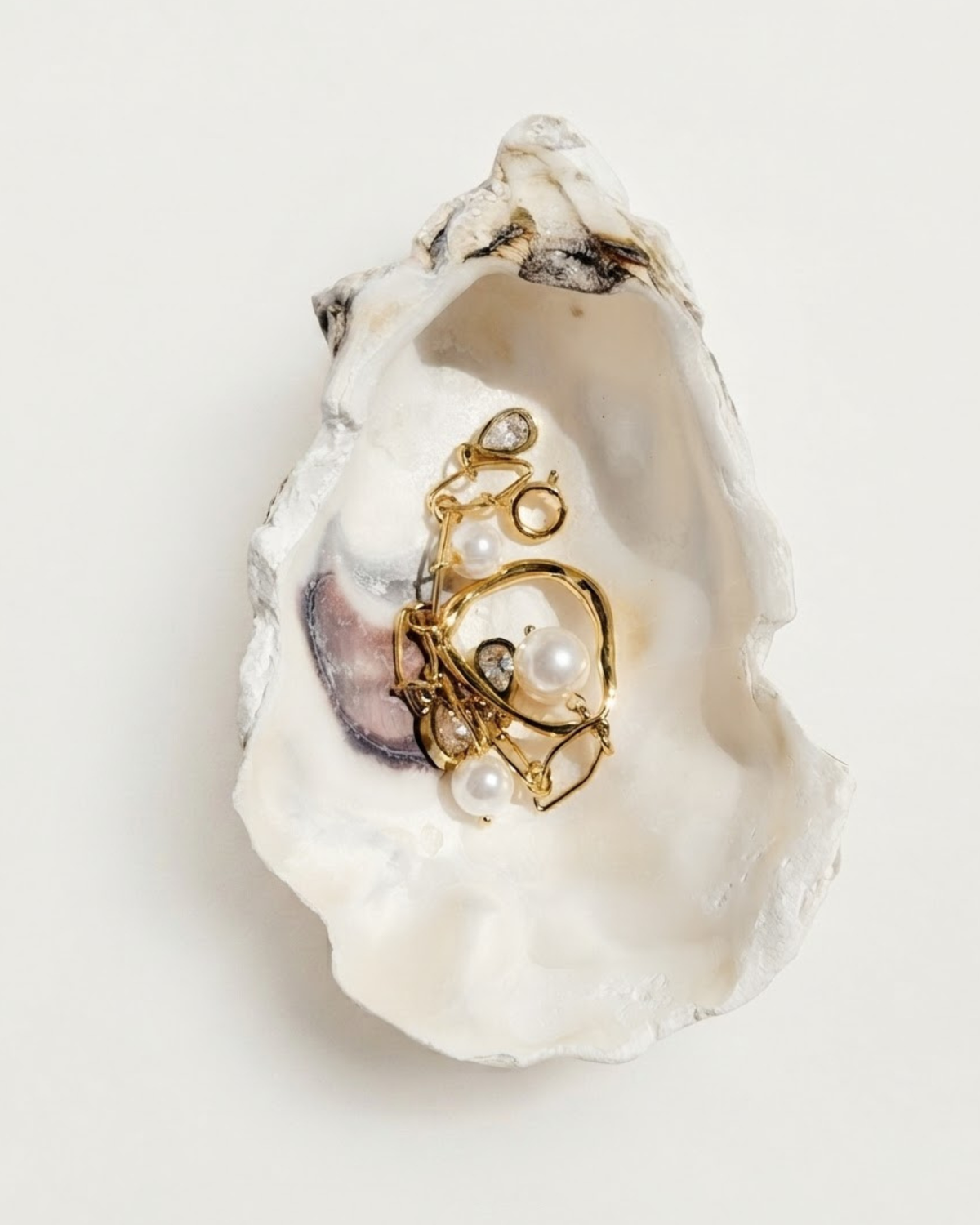Gold Bag Charm -  Detailansicht einer geöffneten Austernschale, die als Schmuckschale dient und einen goldenen Anhänger verziert mit glänzenden Perlen und kleinen tropfenförmigen Schmucksteine enthält.