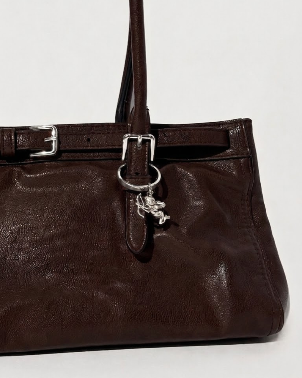 Silber BagBit - Aufnahme einer dunkelbraunen Ledertasche, verziert mit einem detaillierten silbernen Cupid-Anhänger.