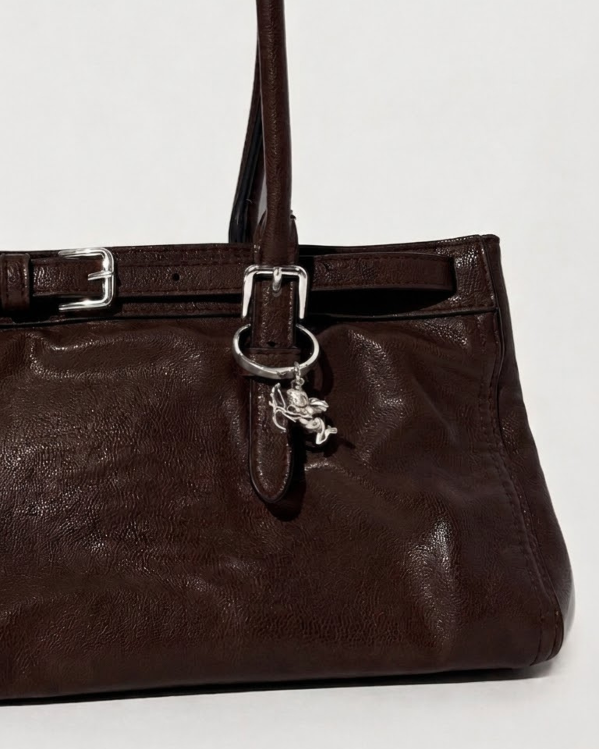 Silber BagBit - Aufnahme einer dunkelbraunen Ledertasche, verziert mit einem detaillierten silbernen Cupid-Anhänger.
