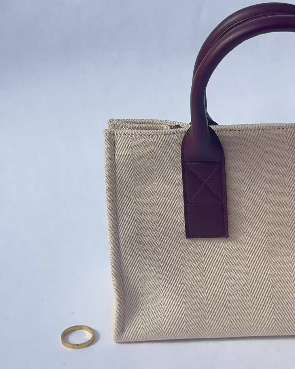 Silber Bag Clip - Hände mit hellgelben Fingernägeln und Schmuck befestigen einen goldenen Bag Clip (Ring-Anhänger) am braunen Ledergriff einer hellen, gemusterten Stofftasche.